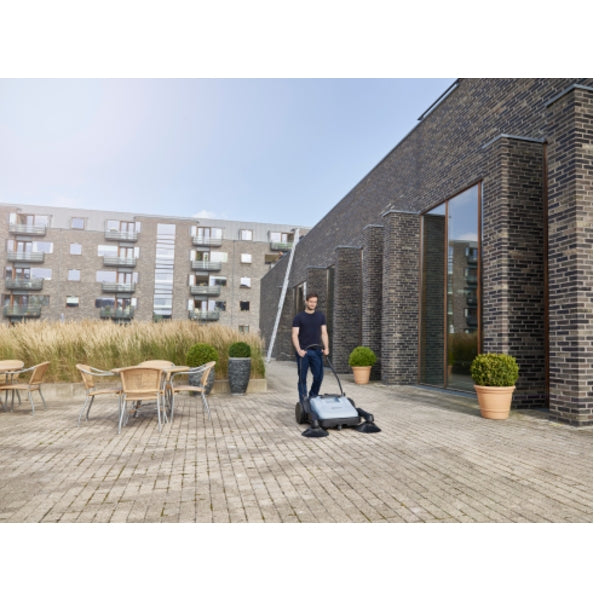 Person using a Nilfisk SW250 Walk Behind Sweeper in courtyard with buildings in the background