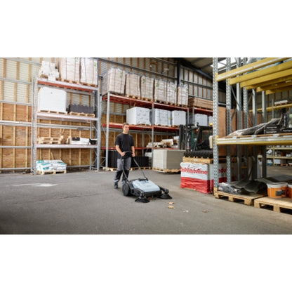 Person operating a Nilfisk SW250 Walk Behind Sweeper in a warehouse setting