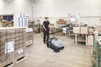 Person operating a Nilfisk SW750 Walk-behind Sweeper cleaning machine in a warehouse setting
