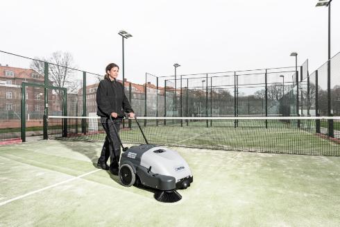 Person operating a Nilfisk SW750 Walk-behind Sweeper on a tennis court