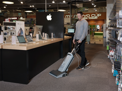 Person using a Nilfisk VU500 Upright Vacuum Cleaner in a store setting with laptops on display.