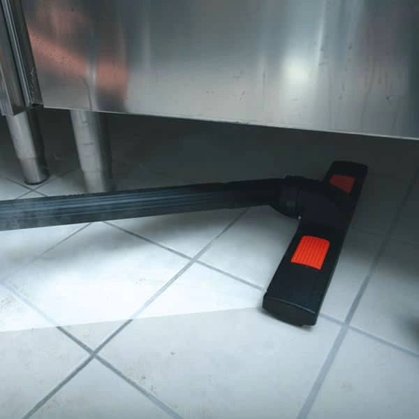 Black and red cleaning tool on a tiled floor with a metallic surface in the background