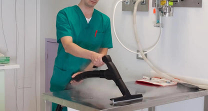 Person in green scrubs using a Novaltec Black Hawk Virucide Steam Cleaning on a table in a clinical setting
