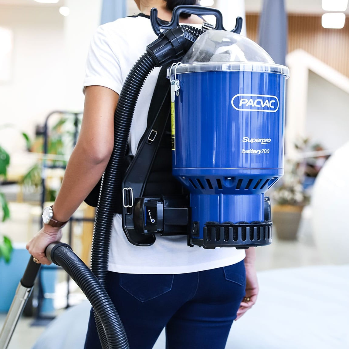 Person carrying a blue backpack vacuum cleaner with 'Pacvac' branding.