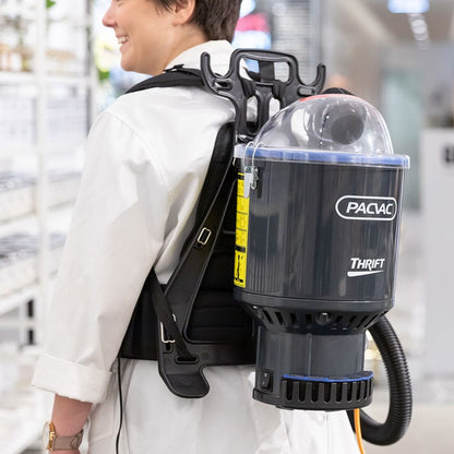 Person wearing a backpack with a Pacvac Thrift vacuum cleaner in an indoor setting.