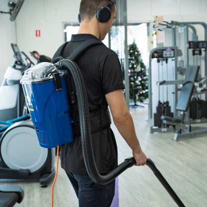 Person using a backpack vacuum cleaner in a gym setting