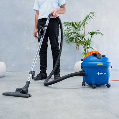 Person using a Pacvac Glide 300 Barrel Vacuum Cleaner with a blue barrel on a concrete floor.