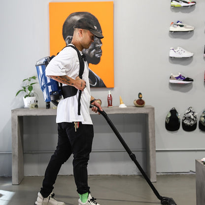 Person using a backpack vacuum cleaner in a room with shelves displaying shoes and hats.