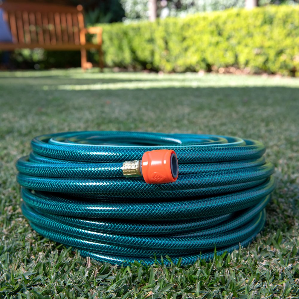 Coiled green garden hose with an orange nozzle on grass