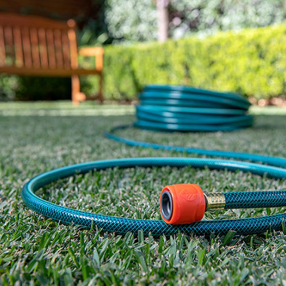 Green garden hose with an orange nozzle on grass, with a blurred background of a garden bench and plants