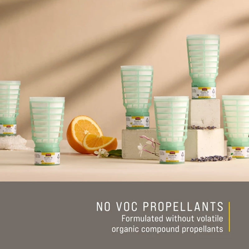Green air freshener containers on a beige surface with an orange and flowers, labeled 'NO VOC Propellants'.