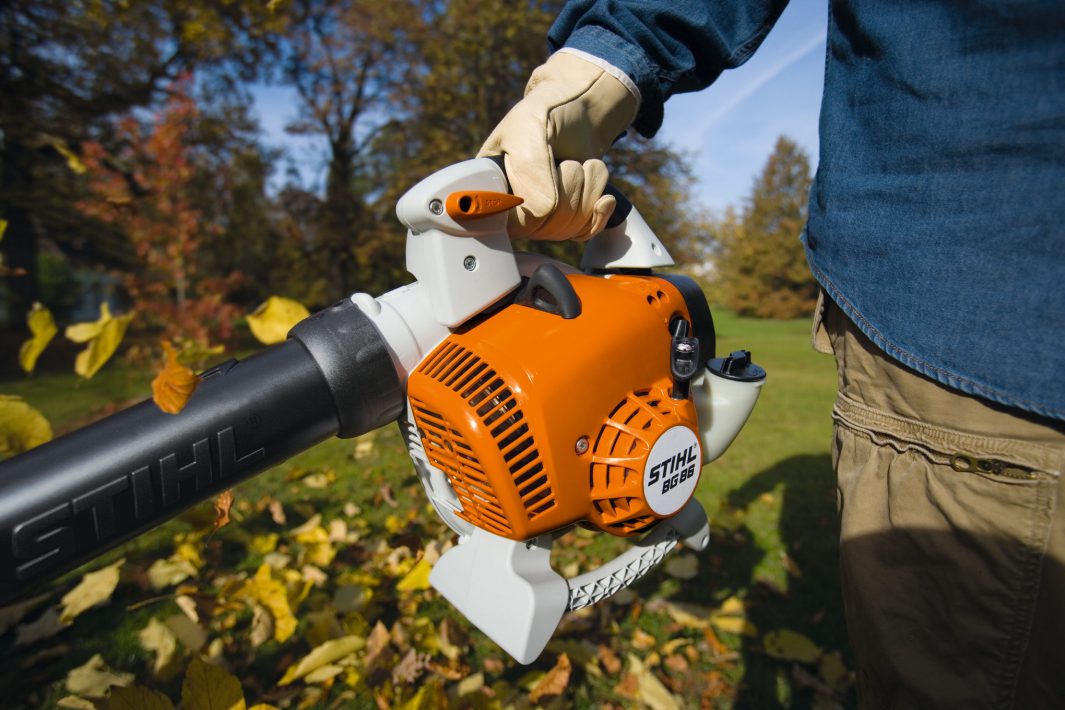 Person using a STIHL leaf blower in an outdoor setting with trees and grass.