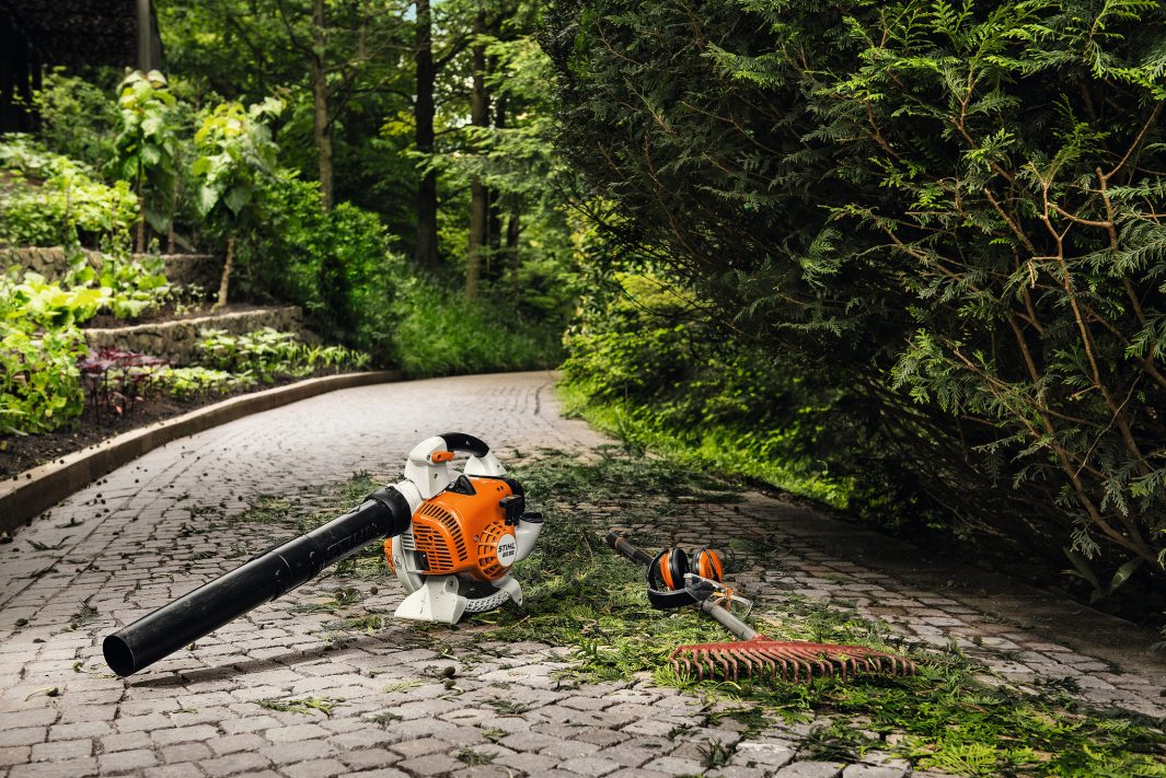 Gardening tools including a STIHL Blower 2 Stroke BG86 leaf blower and brush cutter on a garden path with greenery