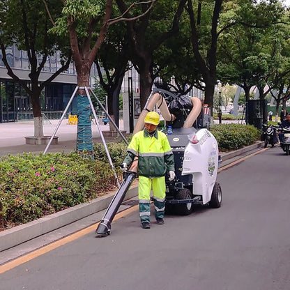 Person in high-visibility clothing using a TSM Ariamatic 240 street cleaning machine on a tree-lined street.
