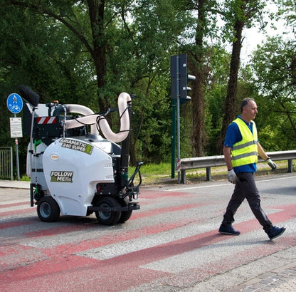 Person in high-visibility clothing walking next to a self-driving TSM Ariamatic 240 on a road.