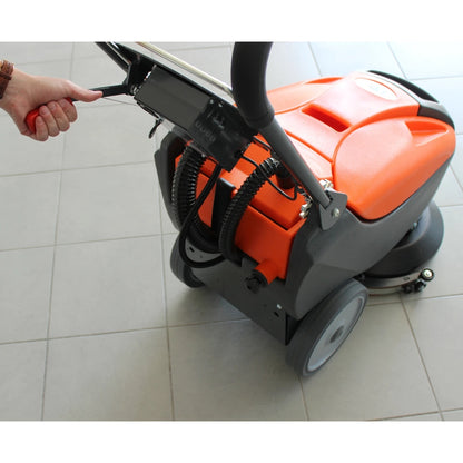 Orange and black floor cleaning machine on a tiled floor with a hand holding onto it.
