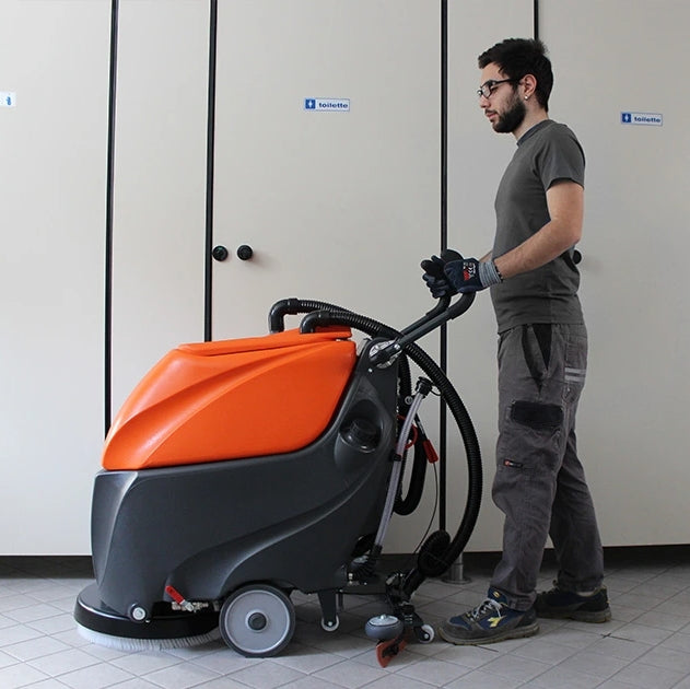 Person operating a TSM Grande Brio 50B Scrubber Dryer in a room with tiled floors and neutral walls.