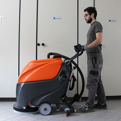 Person operating a TSM Grande Brio 50B Scrubber Dryer in a room with tiled floors and neutral walls.