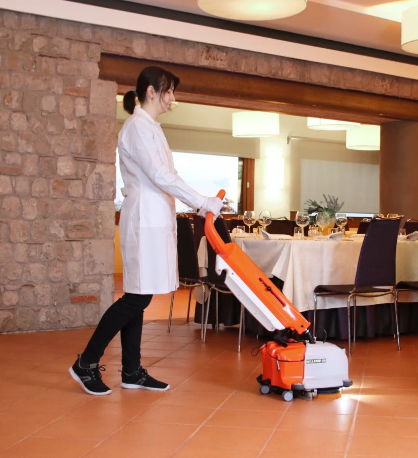 Person pushing an orange and white TSM Willmop 35 Scrubber Dryer in a restaurant setting