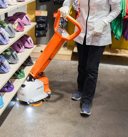Person using a TSM Willmop 35 Scrubber Dryer machine in a store with colorful bike helmets on shelves.