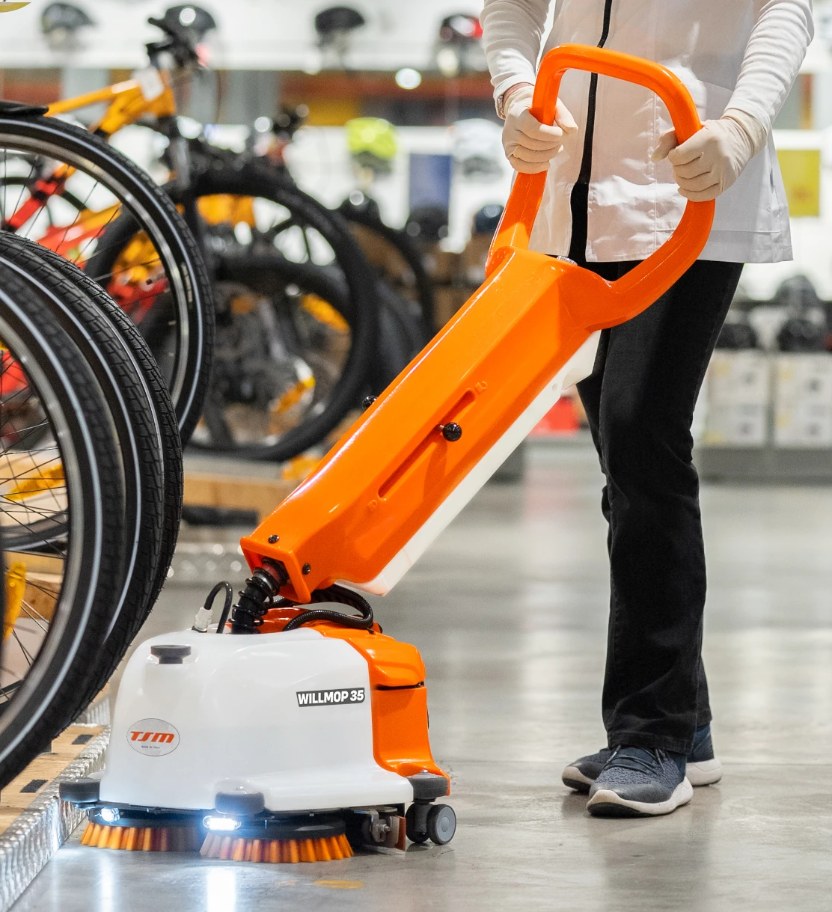 Person operating a TSM Willmop 35 Scrubber Dryer cleaning machine in a retail setting