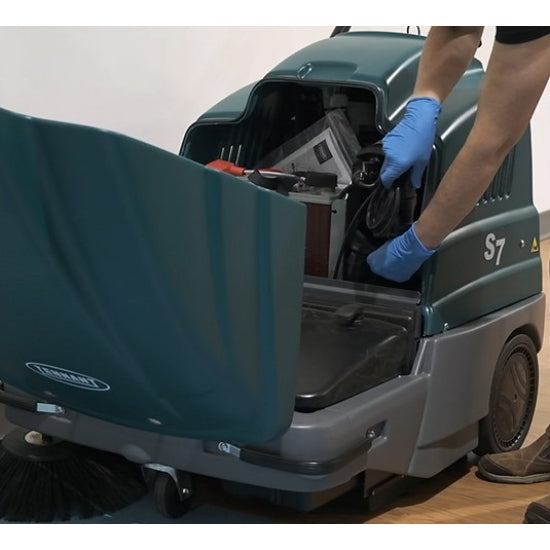 Person cleaning inside a Tennant S7 Battery Sweeper floor cleaning machine with gloves on