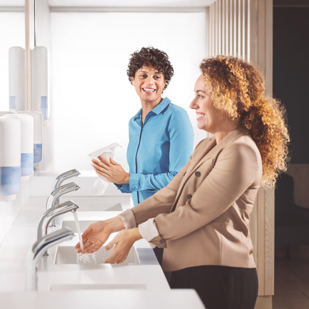 Two women washing hands at a sink in a modern bathroom.