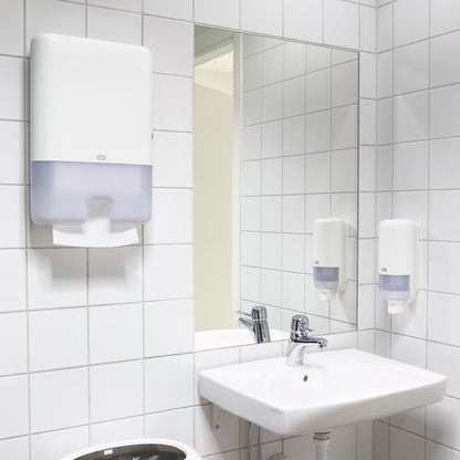 Bathroom with white tiled walls, sink, paper towel and soap dispensers.